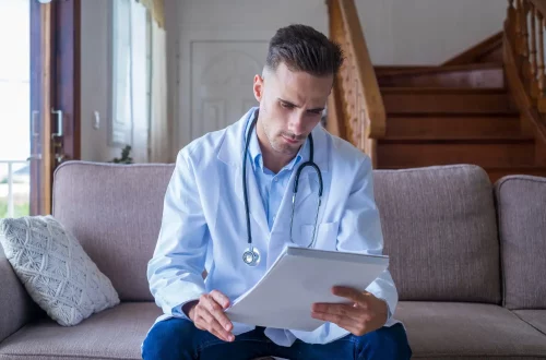 Você deveria se preocupar com o compliance médico: Foto de um médico sentando em um sofá lendo documentos